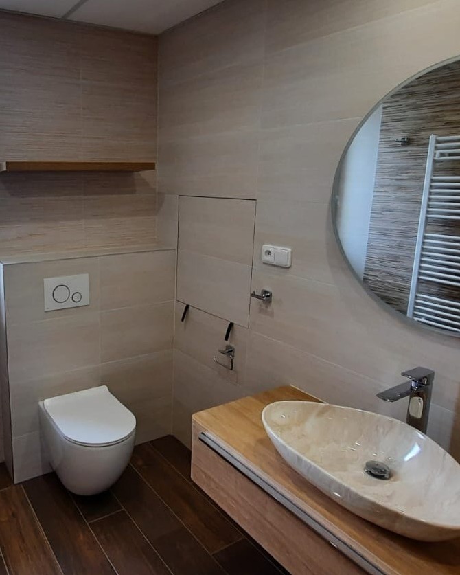 Koupelna plná teplých barev s výraznými prvky jako je podsvícené zrcadlo a mramorové umyvadlo (Most)