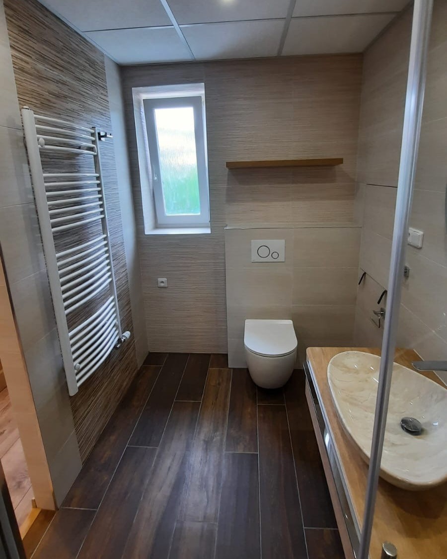 Koupelna plná teplých barev s výraznými prvky jako je podsvícené zrcadlo a mramorové umyvadlo (Most)