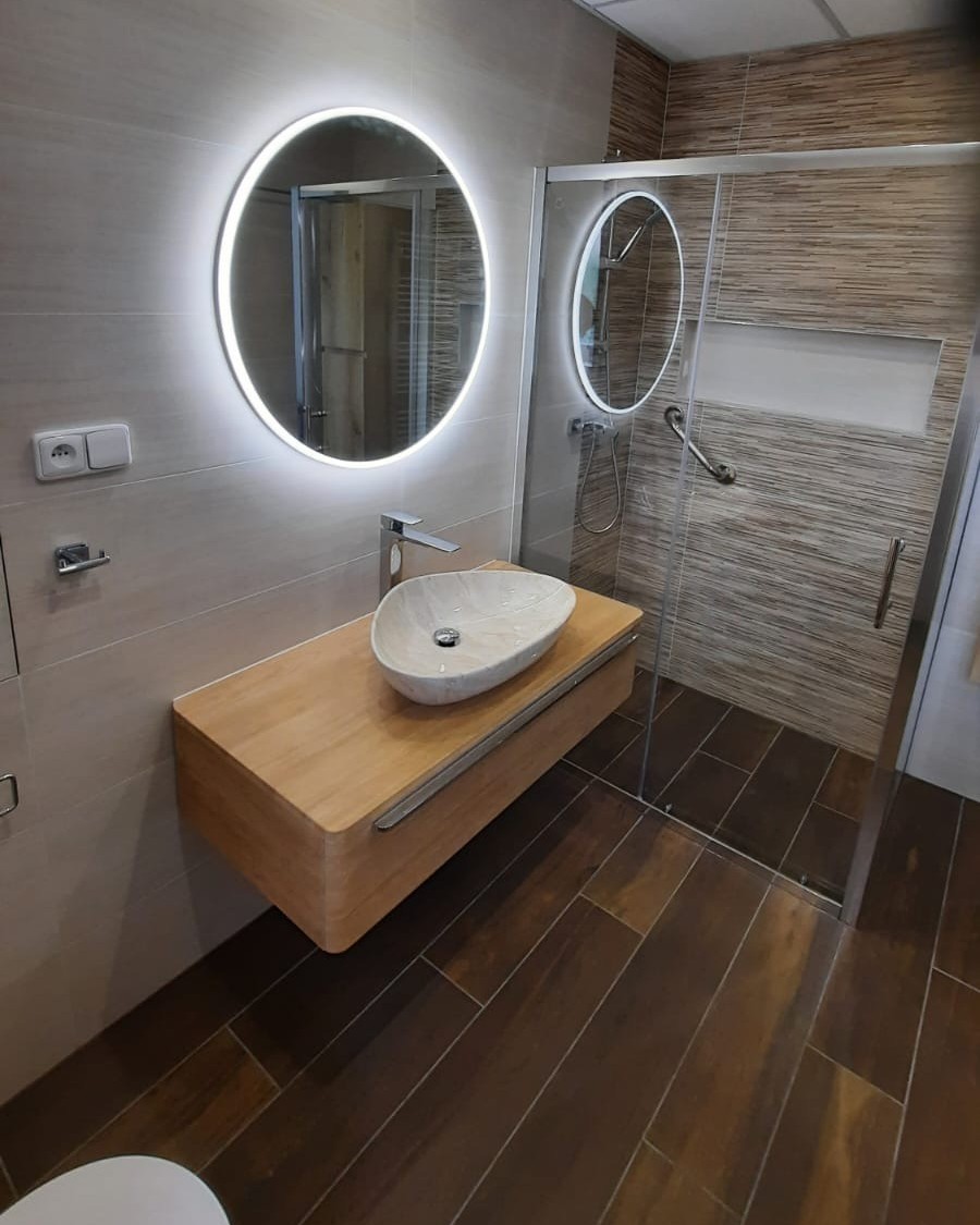 Koupelna plná teplých barev s výraznými prvky jako je podsvícené zrcadlo a mramorové umyvadlo (Most)