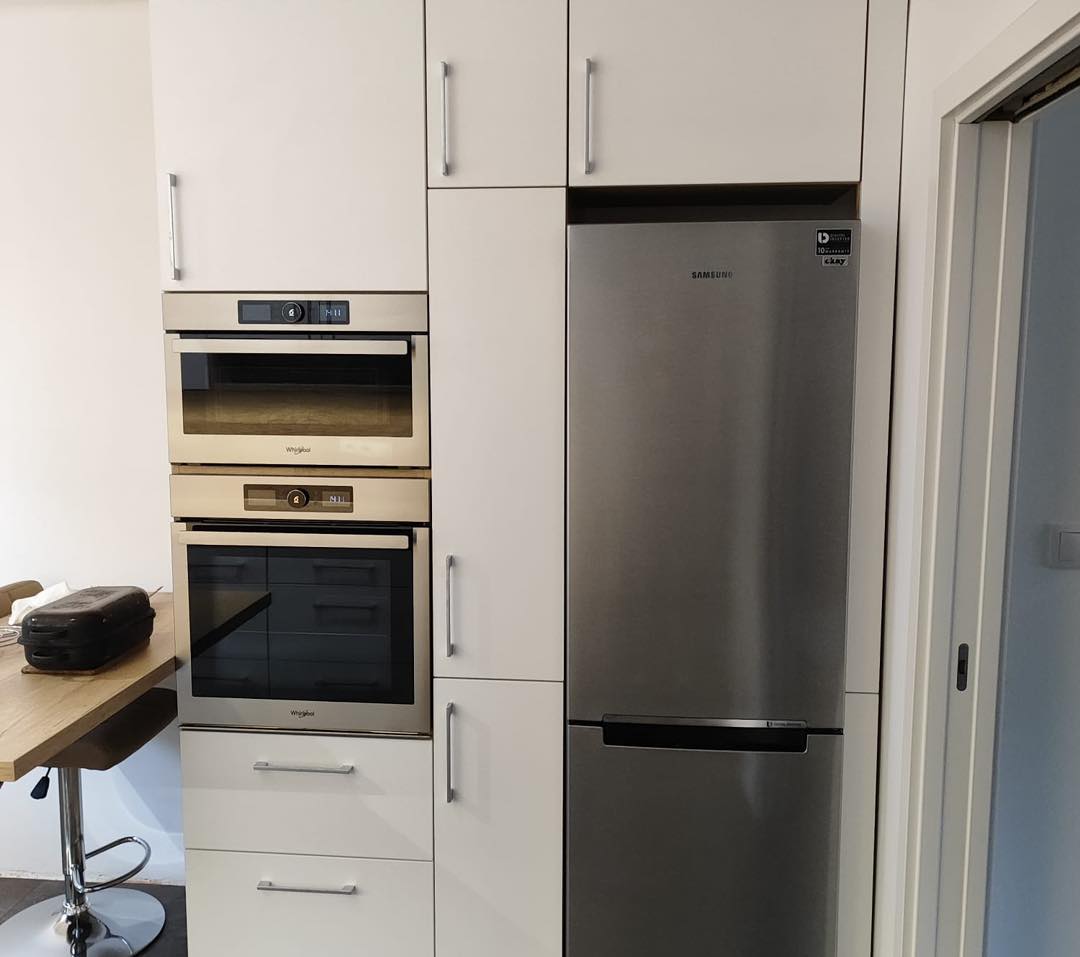 Bílá kuchyň do U s dřevěným dekorem s potravinovou skříní a varnou deskou pod oknem (Most)