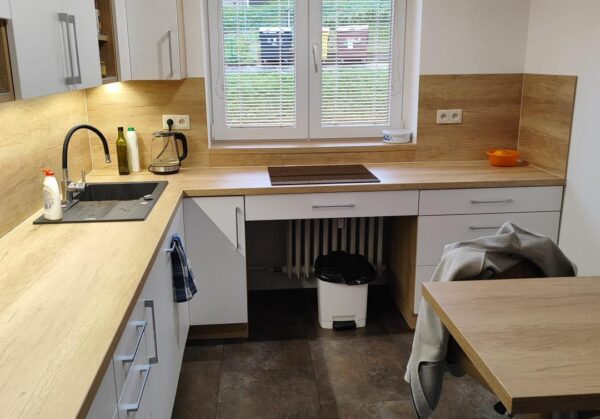 Bílá kuchyň do U s dřevěným dekorem s potravinovou skříní a varnou deskou pod oknem (Most)