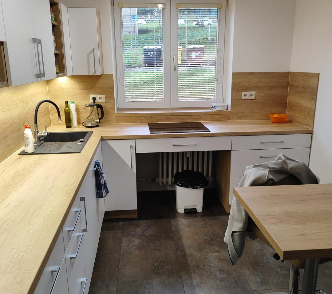 Bílá kuchyň do U s dřevěným dekorem s potravinovou skříní a varnou deskou pod oknem (Most)