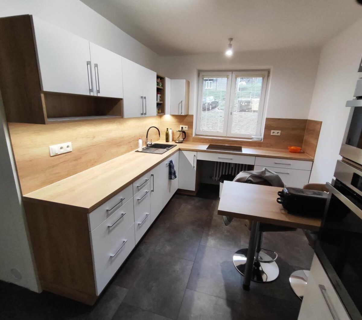 Bílá kuchyň do U s dřevěným dekorem s potravinovou skříní a varnou deskou pod oknem (Most)