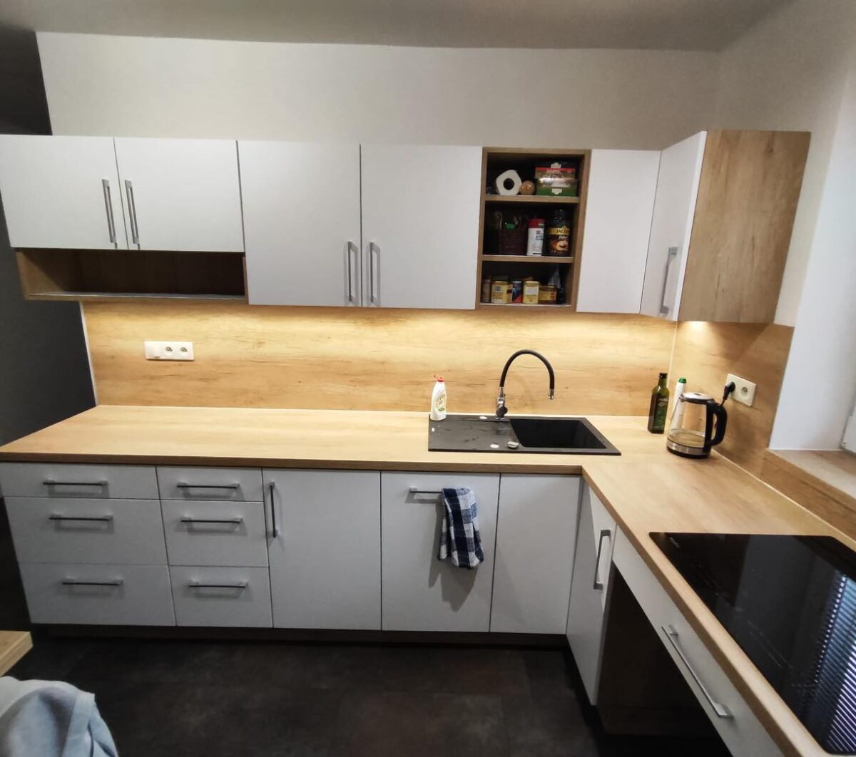 Bílá kuchyň do U s dřevěným dekorem s potravinovou skříní a varnou deskou pod oknem (Most)